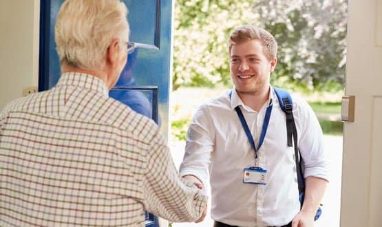 A male healthcare worker greets an elderly man at home